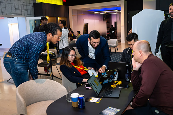 People gathered around a table with laptops in a workspace, engaged in discussion.